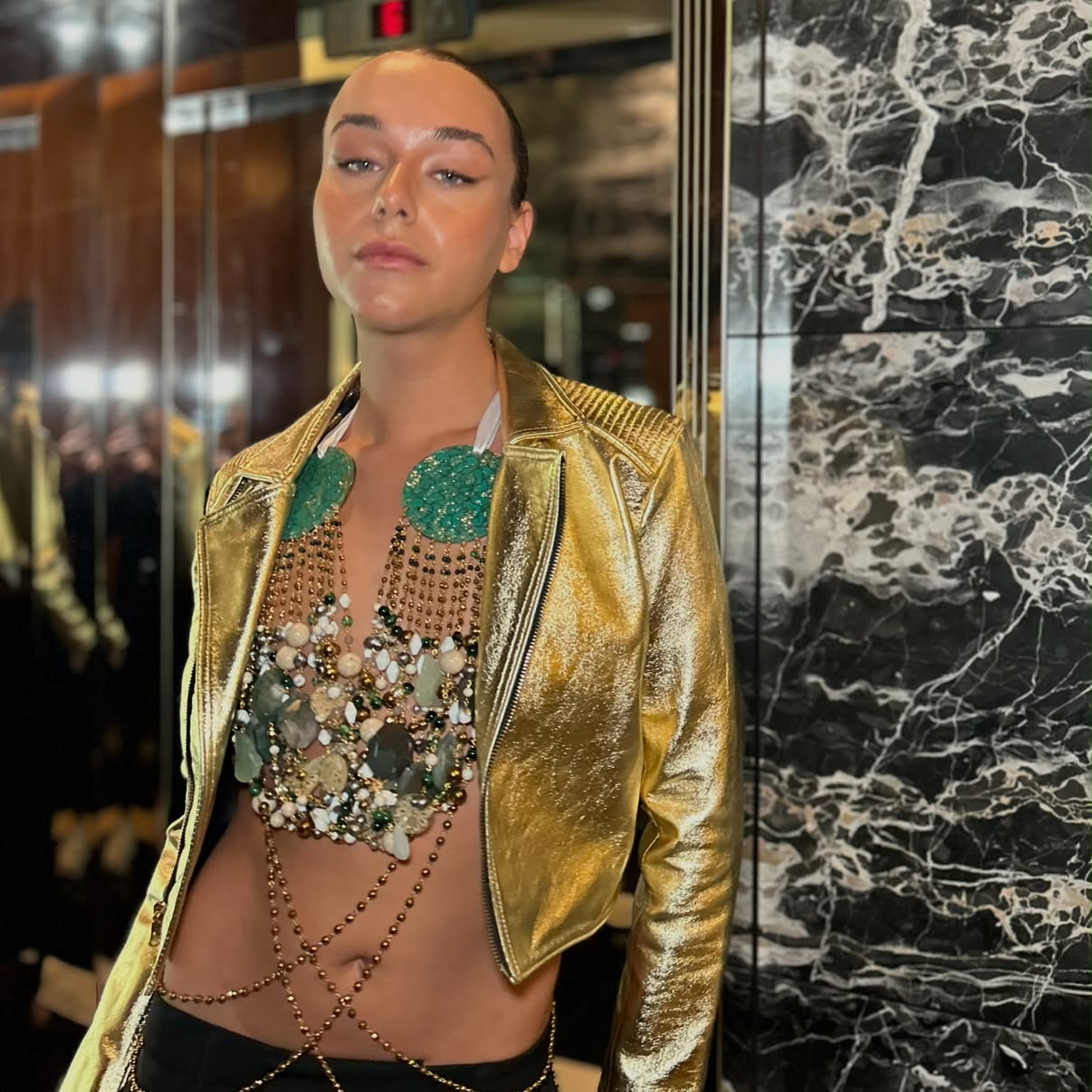 Editorial makeup: sculpted, glowing skin and a slicked-back bun, model in a gold leather jacket against black marble