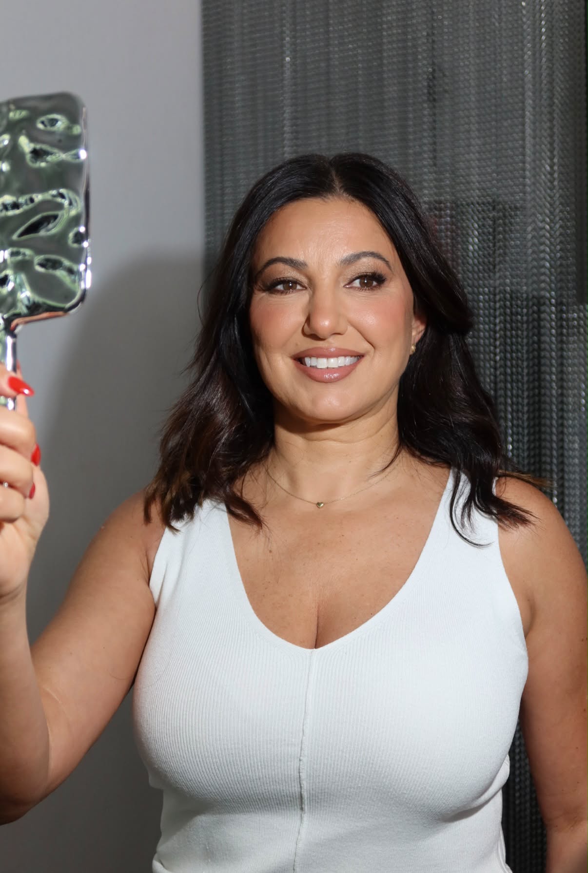 Soft glam: client smiling at her finished look in a hand mirror